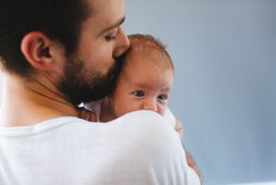 Ein Vater hält sein kleines Baby in den Armen und gibt ihm einen Kuss auf die Schläfe | © AleksandarNakic - Getty Images/iStockphoto